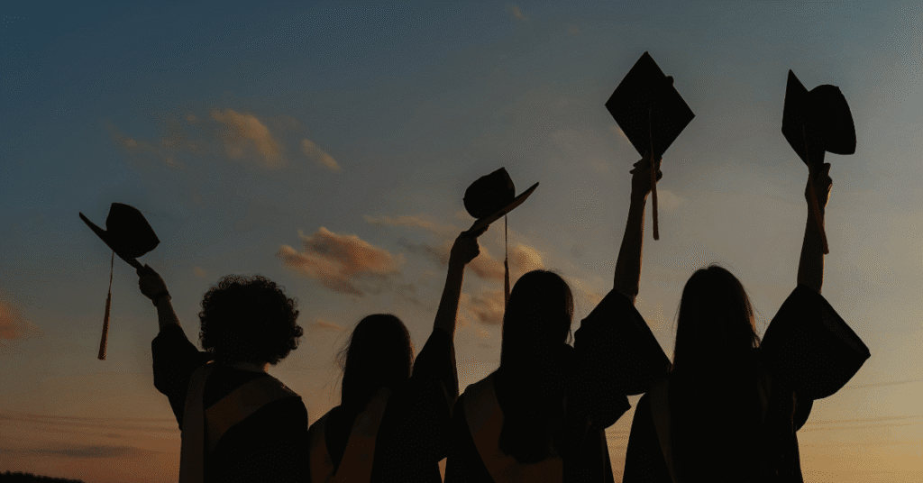 Wisudawan mengangkat topi toga, simbol kelulusan melalui student loan